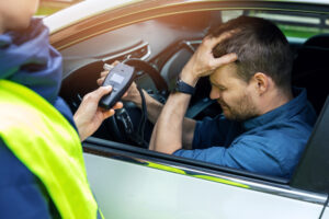 sad drunk man sitting in the car after police alcohol test with alcometer