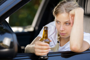 drunk woman driving and holding beer bottle inside a car